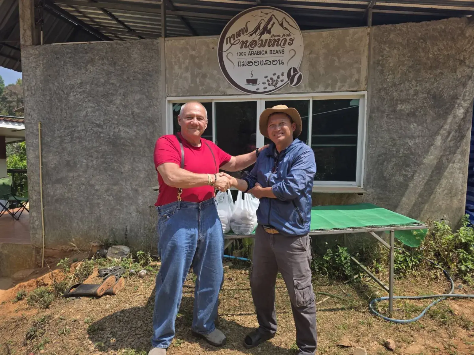 Jack and Manop shaking hands at the HomHoh Coffee sign